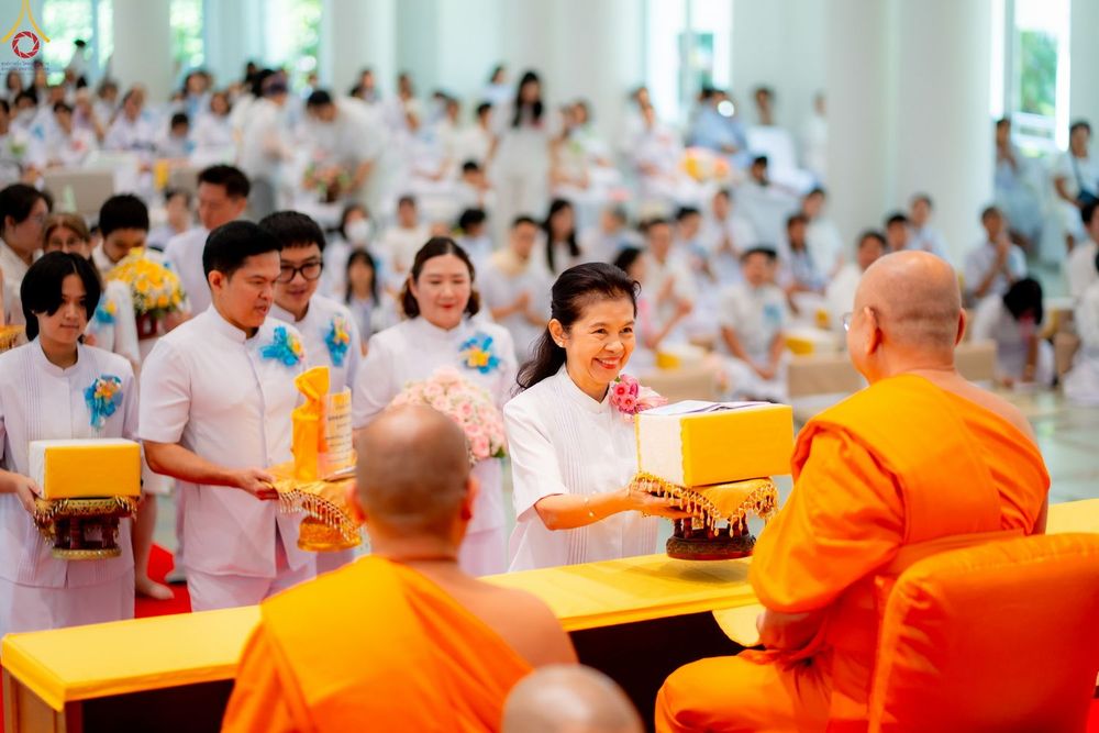 ผู้หญิงในชุดสีขาวกำลังถวายสังฆทานแด่พระสงฆ์ในงานบุญที่มีพุทธศาสนิกชนเข้าร่วมจำนวนมาก