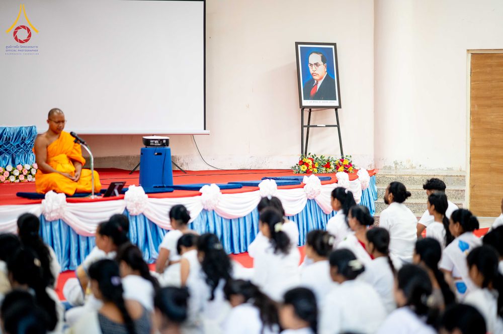 พระภิกษุสงฆ์นั่งบนเวทีแสดงธรรมต่อหน้าผู้เข้าร่วมกิจกรรมที่สวมชุดสีขาวจำนวนมาก