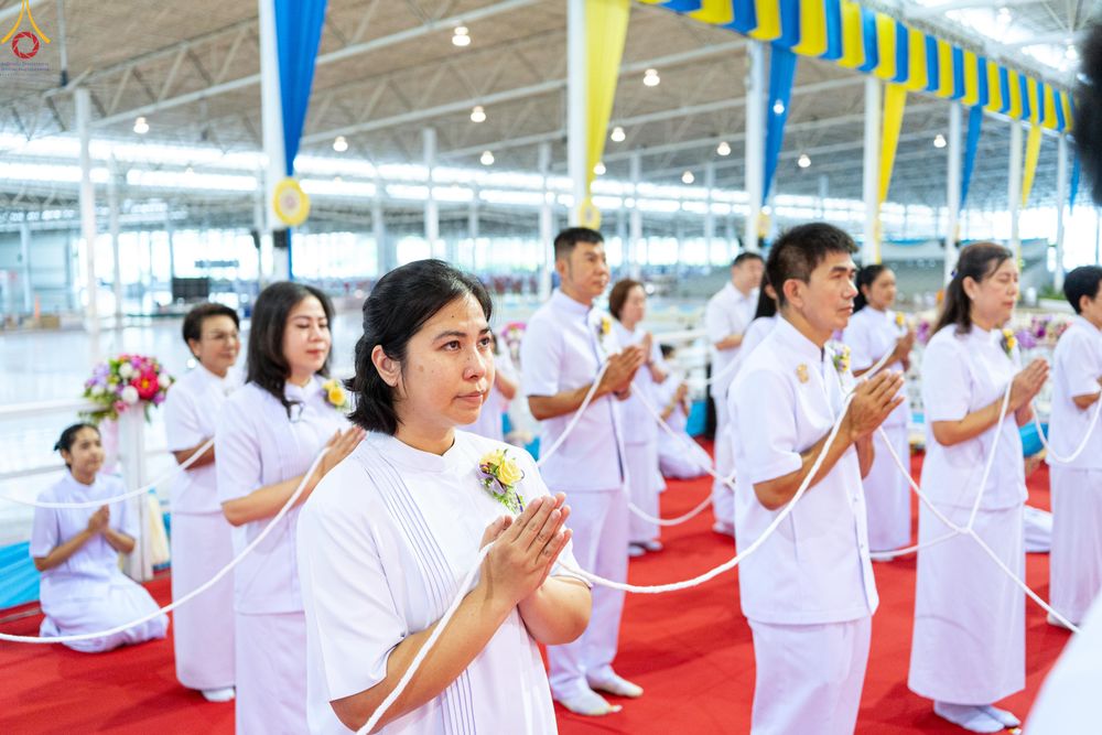 กลุ่มคนสวมชุดขาวกำลังถือสายสิญจน์และพนมมือในพิธีทางศาสนา