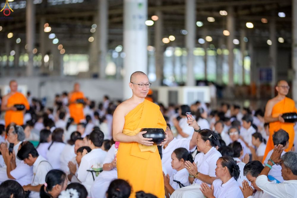 พระภิกษุถือบาตรเดินในพิธีตักบาตรท่ามกลางพุทธศาสนิกชนชุดขาว
