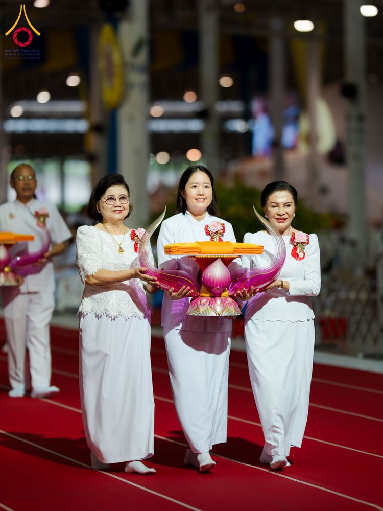 กลุ่มพุทธศาสนิกชนสวมชุดขาวถือพานพุ่มผ้าไตรเดินบนพรมแดงในพิธีทางศาสนา