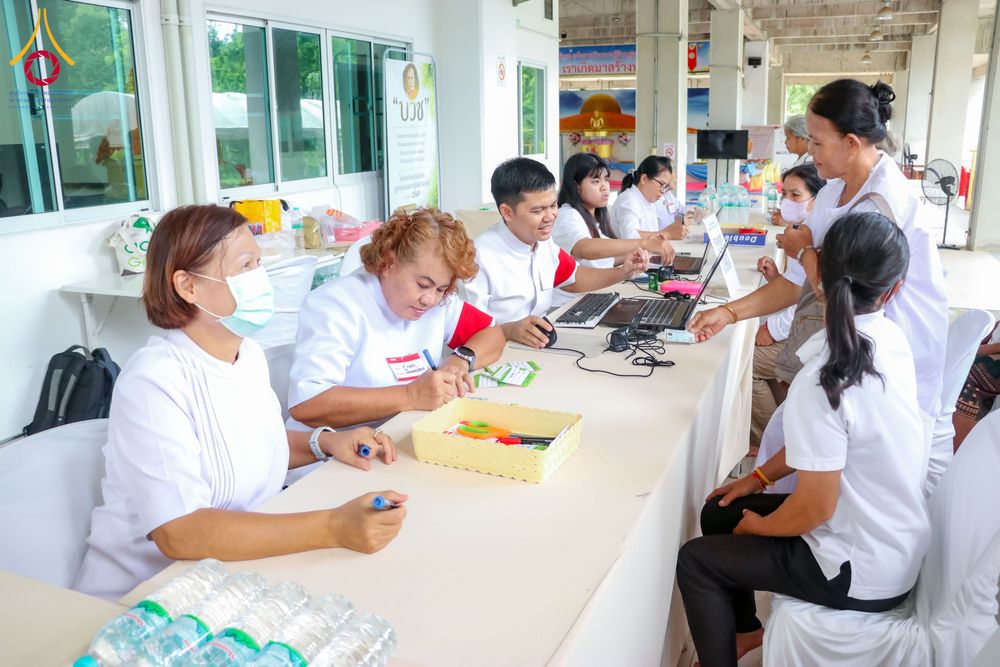 ผู้คนสวมชุดสีขาวกำลังลงทะเบียนกับเจ้าหน้าที่ในจุดรับสมัครโครงการ