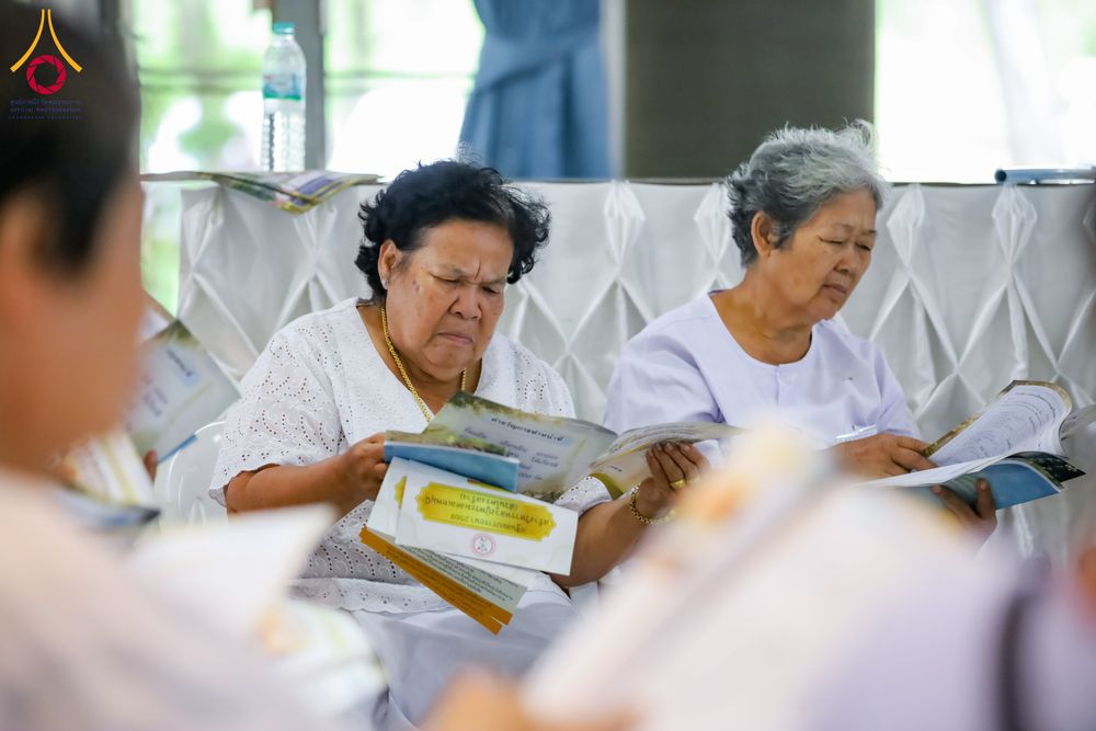 ผู้หญิงสูงอายุสวมชุดสีขาวกำลังอ่านหนังสือในกิจกรรมอบรม