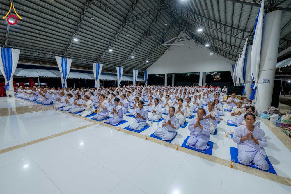 กลุ่มผู้เข้าร่วมโครงการอบรมปฏิบัติธรรมนั่งพนมมือบนเบาะรองนั่งภายในอาคาร