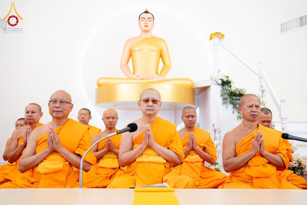 กลุ่มพระภิกษุสงฆ์นั่งพนมมือสวดมนต์หน้าพระพุทธรูปสีทอง