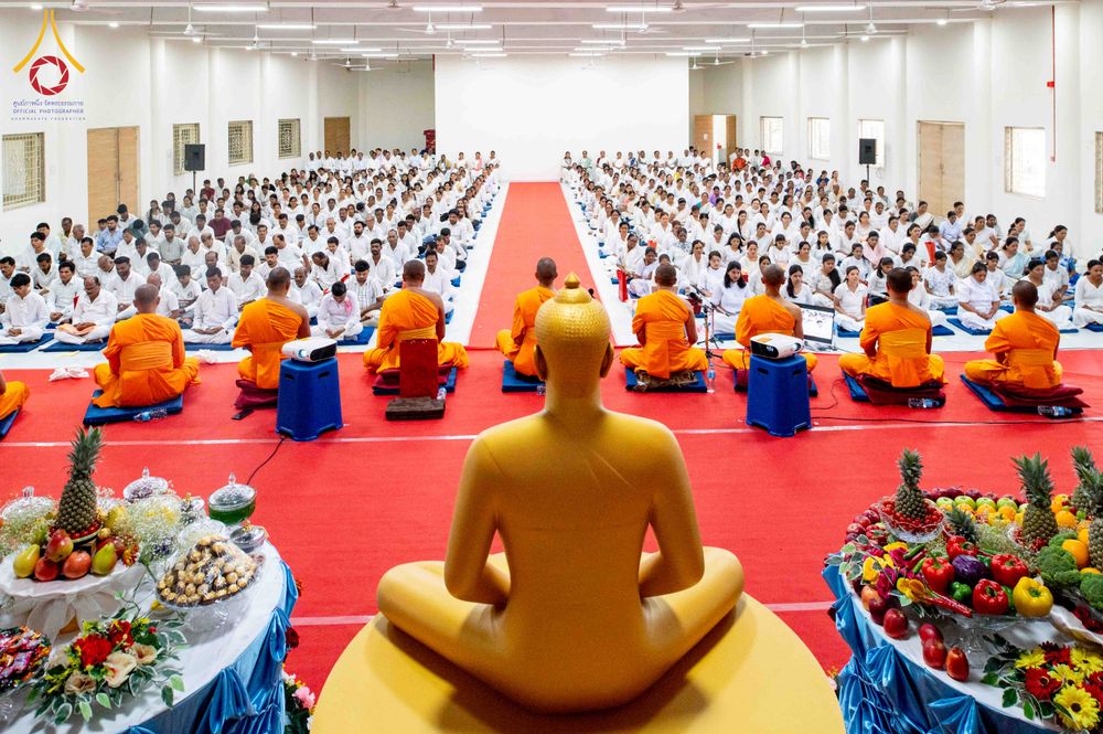 พระพุทธรูปสีทองหันหน้าเข้าหาพุทธศาสนิกชนจำนวนมากที่นั่งเรียงแถวในหอประชุมเพื่อร่วมพิธีทางศาสนา