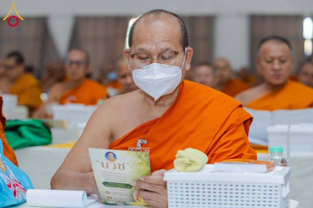 พระภิกษุสวมจีวรสีส้มและหน้ากากอนามัยกำลังอ่านเอกสารในงานสัมมนา