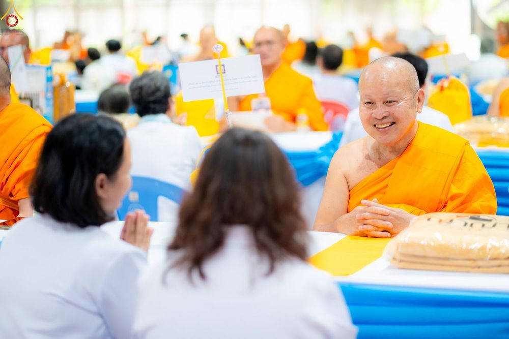 พระสงฆ์ยิ้มแย้มขณะสนทนากับพุทธศาสนิกชนชุดขาวในงานบุญ