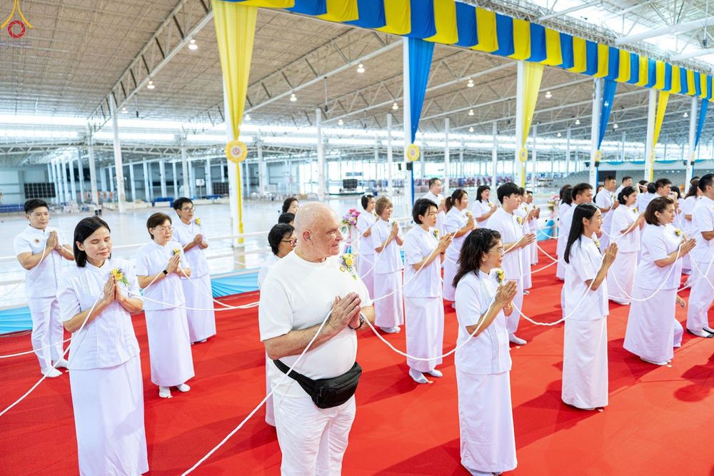 กลุ่มคนสวมชุดขาวถือสายสิญจน์พนมมือประกอบพิธีกรรมทางศาสนาภายในอาคาร