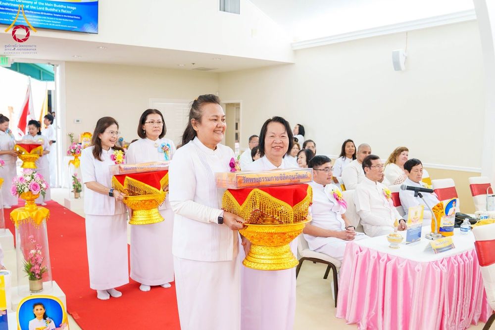 กลุ่มสาธุชนชุดขาวถือพานพุ่มผ้าป่าเดินในแถวภายในอาคารเพื่อร่วมพิธีทางศาสนา