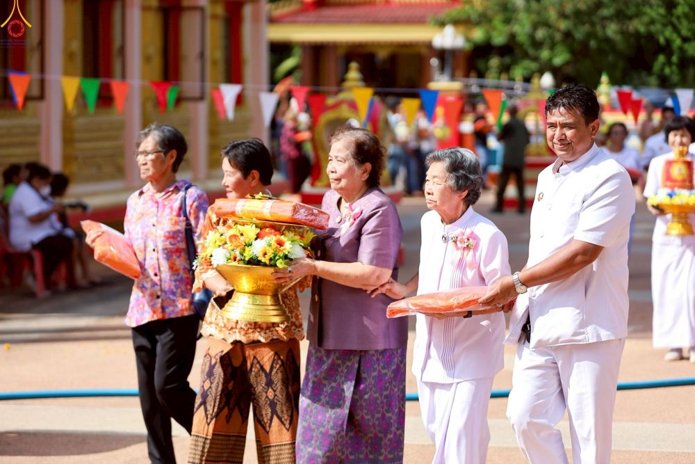 กลุ่มพุทธศาสนิกชนชายหญิงเดินร่วมขบวนแห่กฐิน ถือพานดอกไม้และผ้าไตรจีวรในงานบุญ