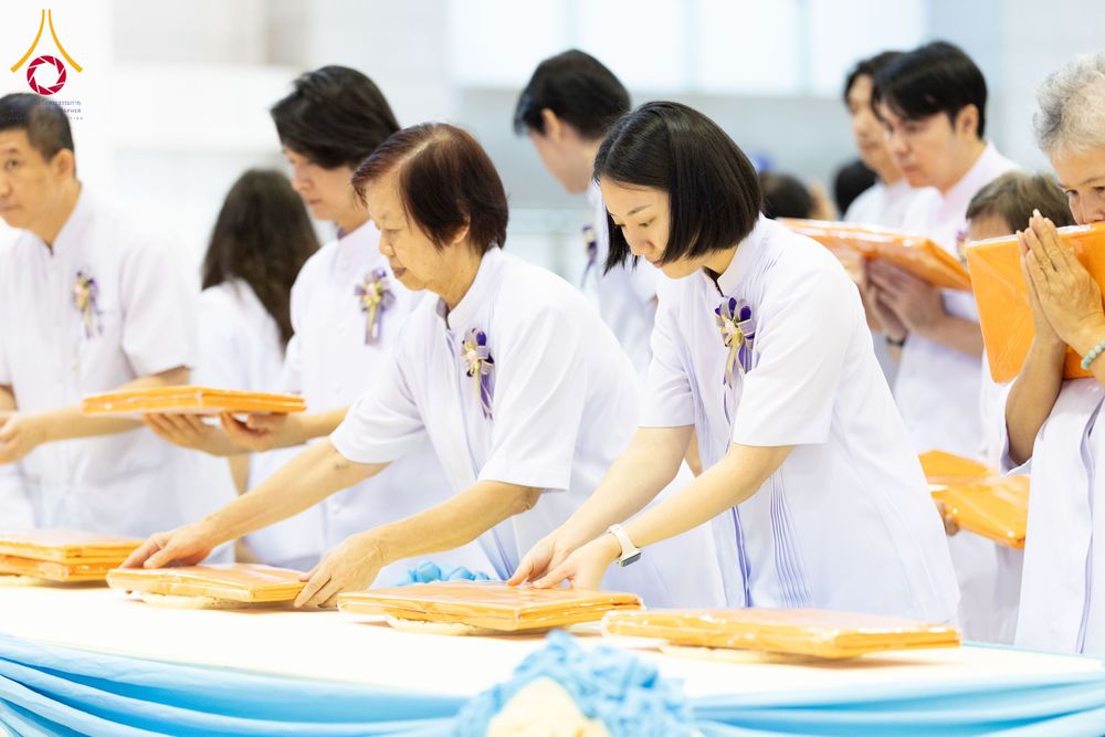 กลุ่มคนสวมชุดขาวกำลังวางผ้าไตรสีเหลืองทองบนโต๊ะในพิธีทางศาสนา