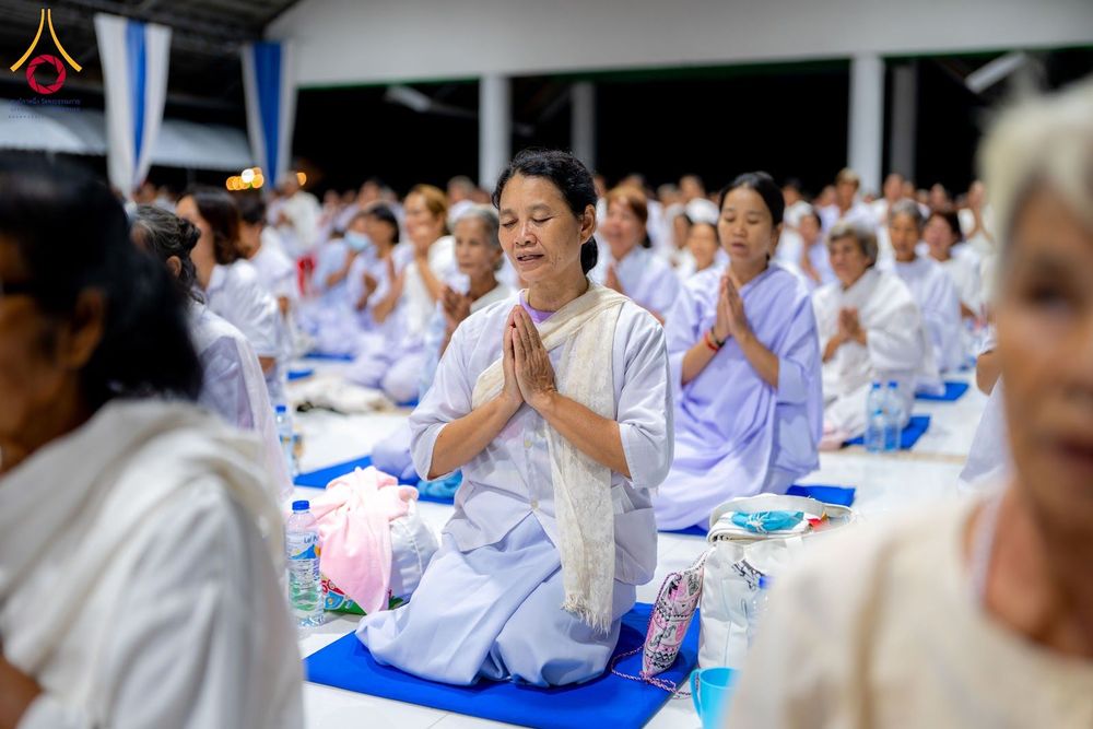 กลุ่มอุบาสิกาแก้วสวมชุดสีขาวนั่งพนมมือปฏิบัติธรรมอย่างสงบในอาคารปฏิบัติธรรม