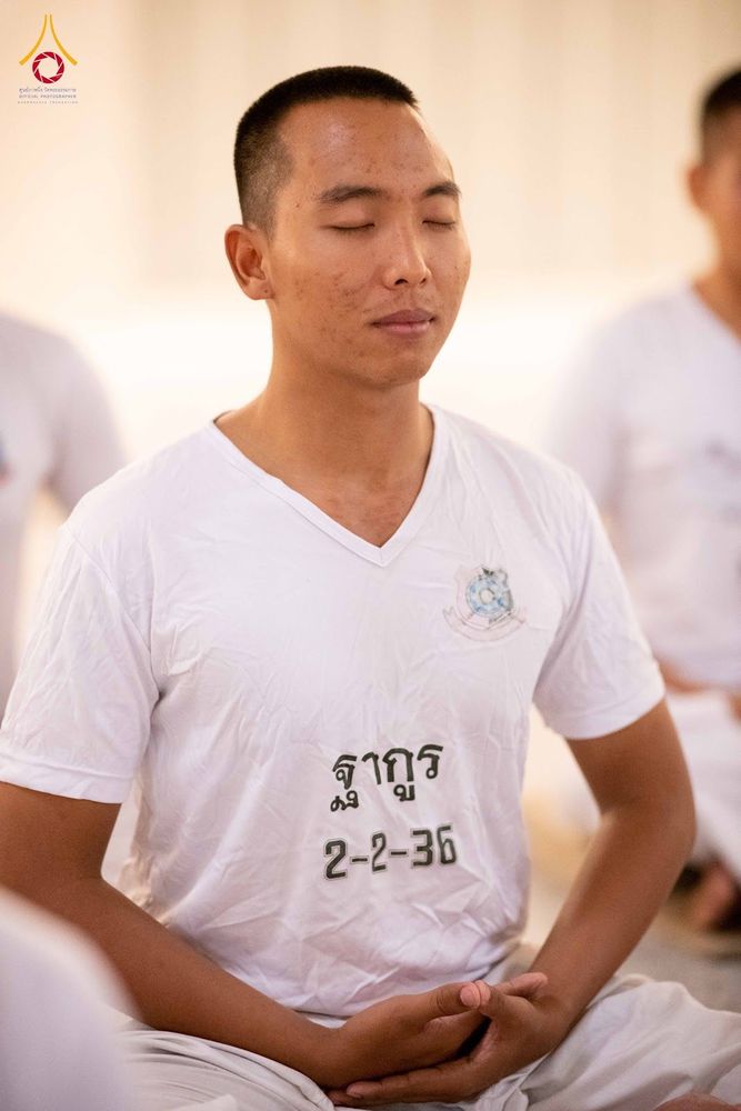 ชายหนุ่มสวมเสื้อสีขาวนั่งหลับตาทำสมาธิในกิจกรรมปฏิบัติธรรม