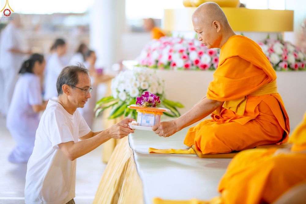 ชายสวมเสื้อสีขาวกำลังประเคนของใส่บาตรแด่พระภิกษุสงฆ์