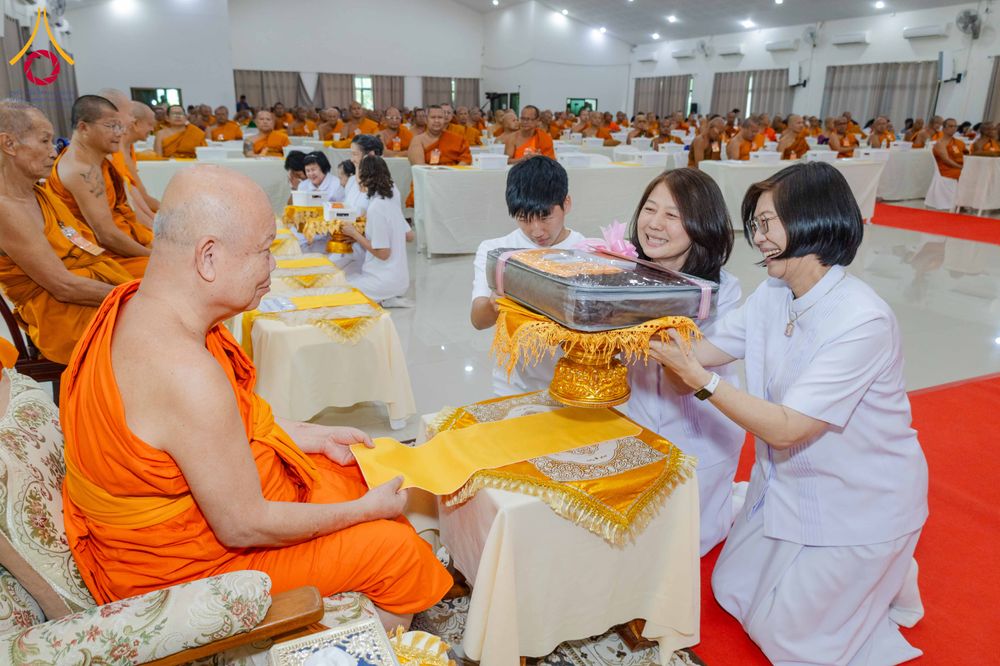 หญิงชุดขาวสองคนกำลังถวายผ้าไตรและเครื่องไทยธรรมแด่พระภิกษุสงฆ์ในงานสัมมนา