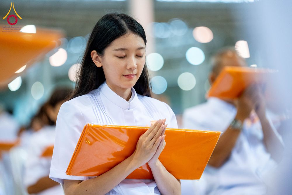 หญิงสาวสวมชุดขาวประนมมือถือผ้าไตรสีส้มในพิธีทางศาสนา