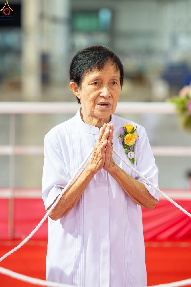 หญิงสูงวัยสวมชุดขาวพนมมือถือสายสิญจน์ในพิธีทางศาสนา