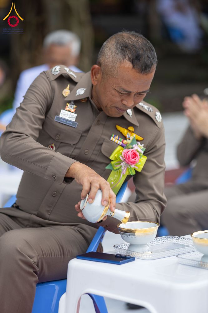 เจ้าหน้าที่ตำรวจในเครื่องแบบกำลังเทน้ำจากกรวยลงในถ้วยเพื่อประกอบพิธีกรวดน้ำ