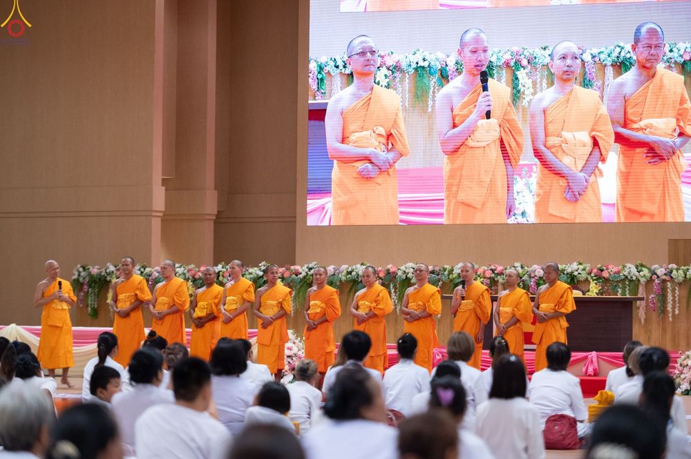 พระภิกษุสงฆ์ยืนบนเวทีในงานสัมมนาโดยมีจอภาพขนาดใหญ่แสดงภาพพระภิกษุกำลังบรรยายธรรม