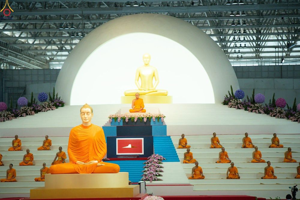 พระภิกษุสงฆ์นั่งสมาธิเรียงรายบนอัฒจันทร์หน้าพระพุทธรูปองค์สีทองภายในอาคาร