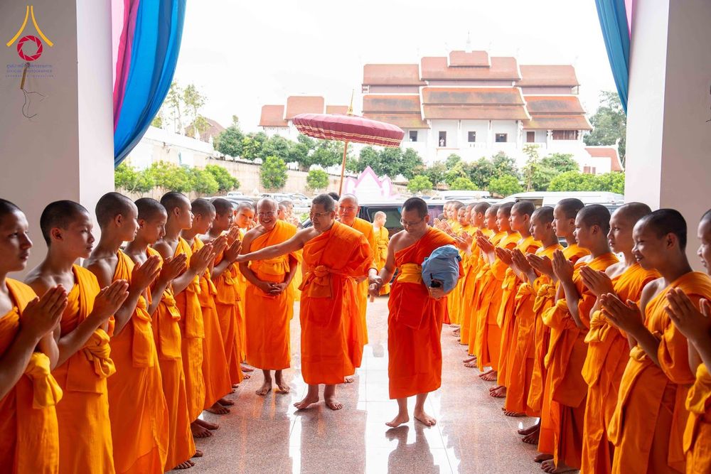 พระภิกษุสงฆ์เดินผ่านแถวสามเณรที่ยืนพนมมือต้อนรับภายในอาคารวัด