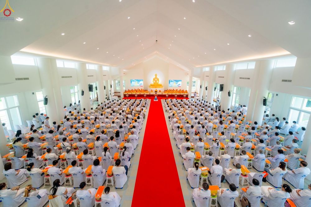 ภาพมุมกว้างภายในอาคารพิธี สาธุชนจำนวนมากสวมชุดขาวนั่งเป็นระเบียบสองฝั่งทางเดินพรมแดง เบื้องหน้ามีคณะสงฆ์และพระพุทธรูปองค์ใหญ่ ในงานบุญครบรอบ 40 ปี ธุดงคสถานล้านนา
