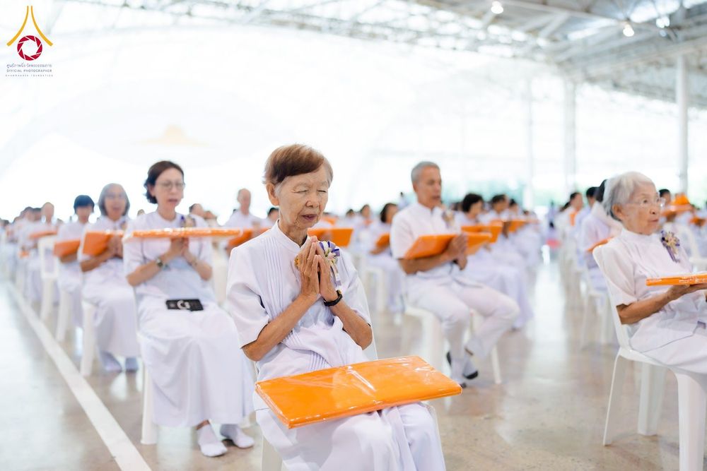 กลุ่มคนสวมชุดขาวนั่งพนมมือประกอบพิธีทางศาสนาภายในอาคาร