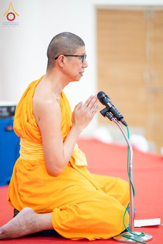 พระภิกษุสงฆ์นั่งพนมมือและพูดผ่านไมโครโฟนบนเวที