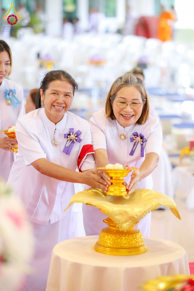 อุบาสิกาแก้วสองท่านสวมชุดสีขาวกำลังถือพานพุ่มดอกไม้สีทองในงานพิธีทางศาสนา