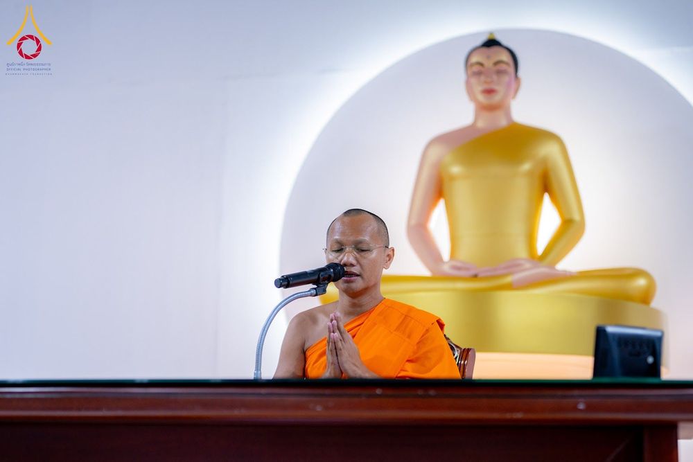 พระภิกษุสงฆ์กำลังประนมมือสวดมนต์หน้าไมโครโฟน โดยมีพระพุทธรูปสีทองเป็นฉากหลัง