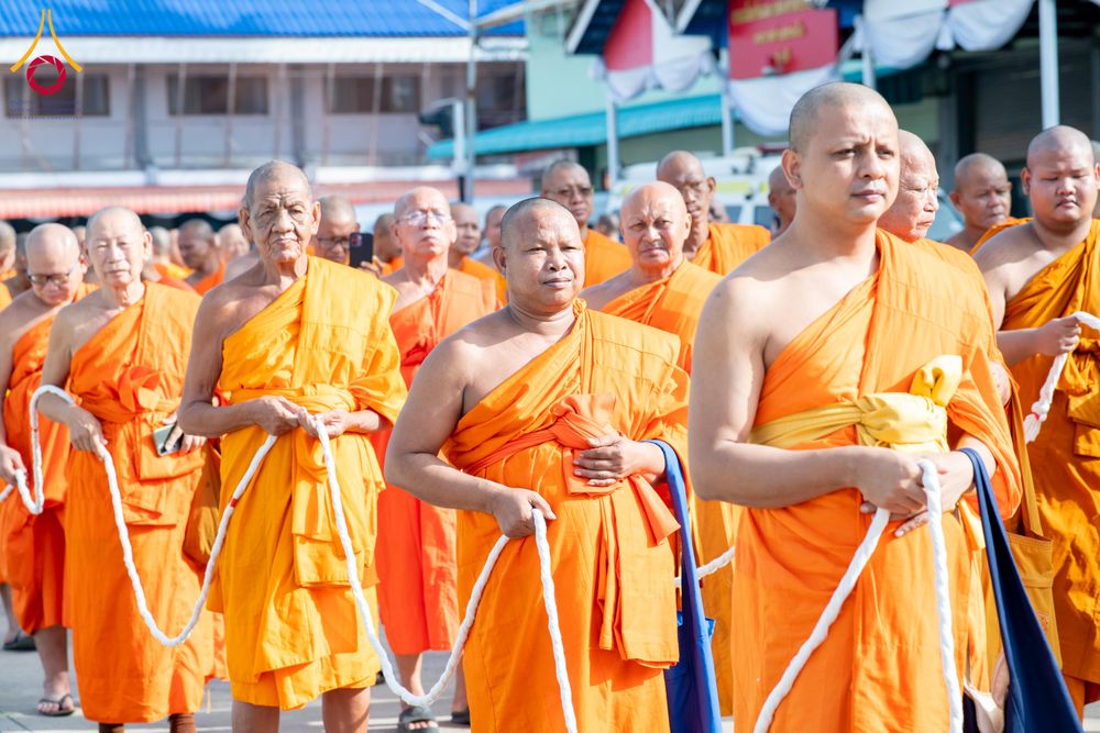 พระภิกษุสงฆ์หลายรูปเดินแถวถือสายสิญจน์ในพิธีทางศาสนา