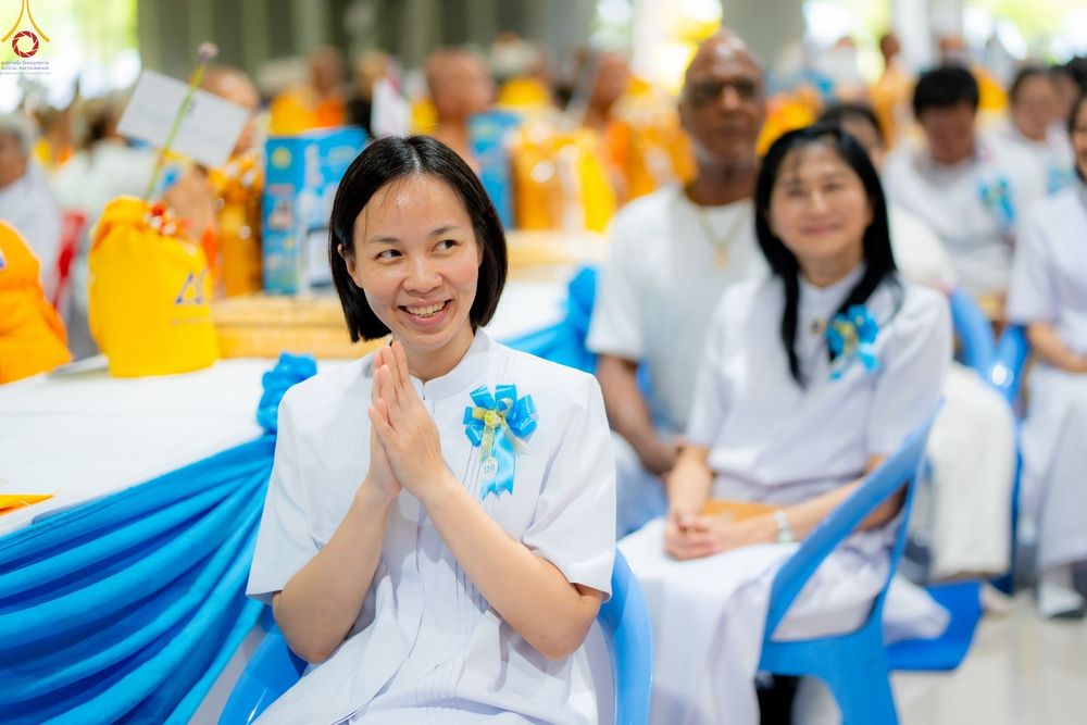 หญิงสาวสวมชุดสีขาวพนมมือยิ้มแย้มในงานบุญ