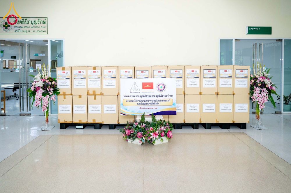 กล่องยาจำนวนมากวางเรียงกันเพื่อเตรียมส่งมอบบริจาค โดยมีป้ายโครงการวางอยู่ด้านหน้าท่ามกลางการประดับตกแต่งด้วยแจกันดอกไม้