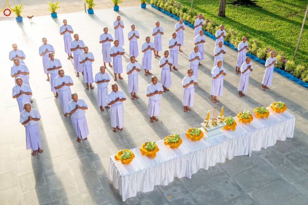 กลุ่มผู้ชายสวมชุดสีขาวกำลังยืนพนมมือประกอบพิธีกรรมทางศาสนาหน้าโต๊ะหมู่บูชา