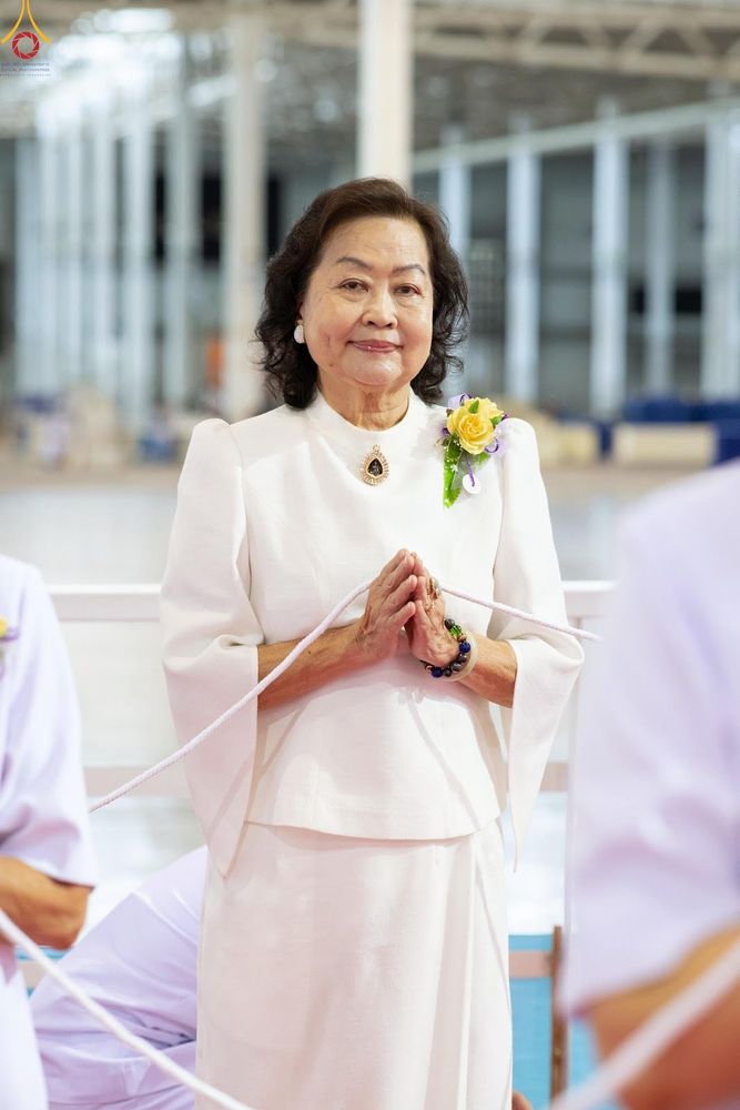 สุภาพสตรีสวมชุดสีขาวประนมมือไหว้ด้วยใบหน้ายิ้มแย้ม