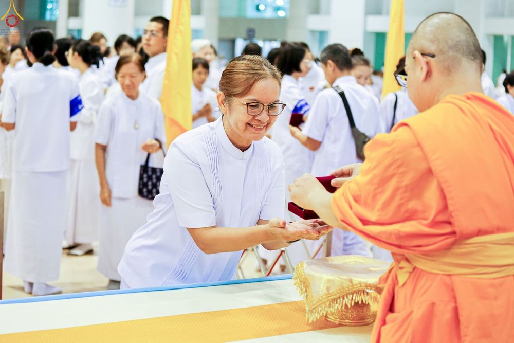 หญิงสวมชุดขาวกำลังรับมอบพระของขวัญจากพระภิกษุสงฆ์ในพิธีการ