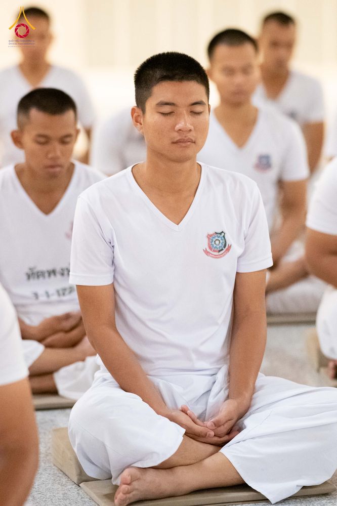 นักเรียนนายสิบตำรวจสวมเสื้อยืดสีขาวนั่งขัดสมาธิหลับตาทำสมาธิในห้องโถง