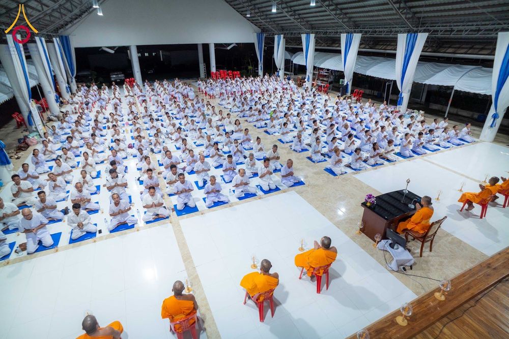 กลุ่มผู้เข้าร่วมโครงการอบรมในชุดสีขาวนั่งสมาธิภายในอาคารปฏิบัติธรรม โดยมีพระภิกษุสงฆ์นั่งเป็นประธานด้านหน้า