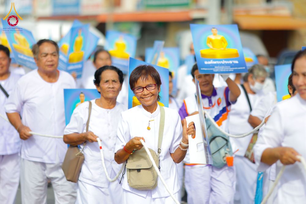 กลุ่มคนสวมชุดขาวถือป้ายรูปพระพุทธรูปและเชือกสีขาวเดินในขบวนพิธีทางศาสนา