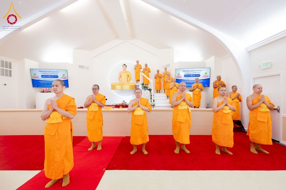 คณะสงฆ์ยืนพนมมือประกอบพิธีกรรมหน้าพระพุทธรูปภายในอาคาร