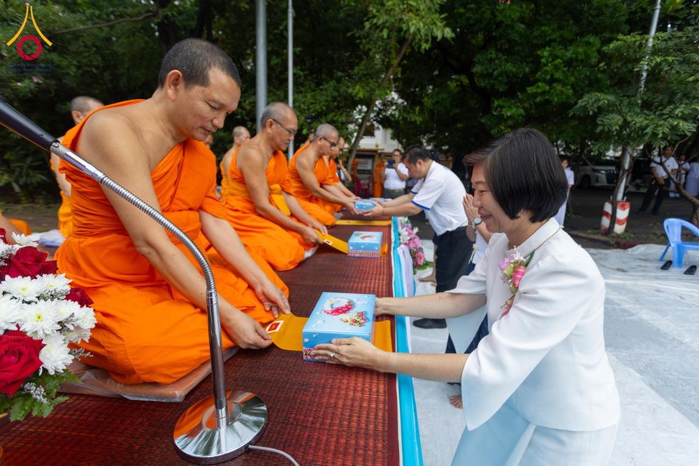 หญิงสวมชุดสีขาวกำลังประเคนของใส่บาตรให้แก่สามเณรในพิธีตักบาตร