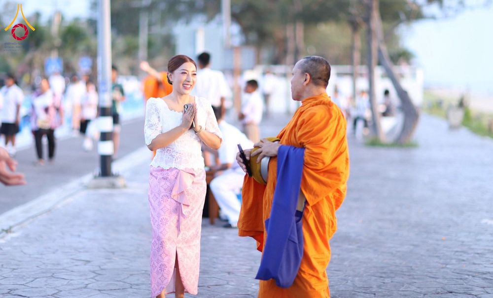 หญิงสาวสวมชุดไทยยกมือไหว้พระสงฆ์ขณะทำบุญตักบาตรริมชายหาด