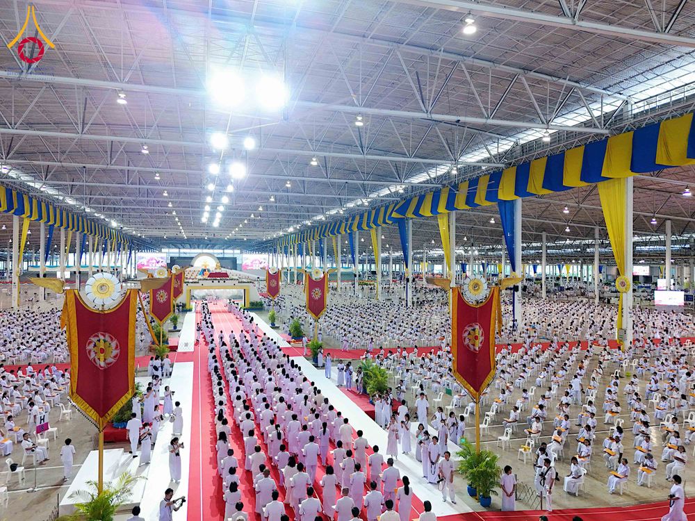 พุทธศาสนิกชนจำนวนมากสวมชุดสีขาวนั่งและยืนเรียงแถวภายในอาคารขนาดใหญ่เพื่อร่วมพิธีทางศาสนา