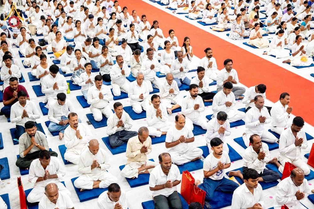 กลุ่มคนสวมชุดสีขาวนั่งพนมมือปฏิบัติธรรมบนเบาะรองนั่งในอาคาร
