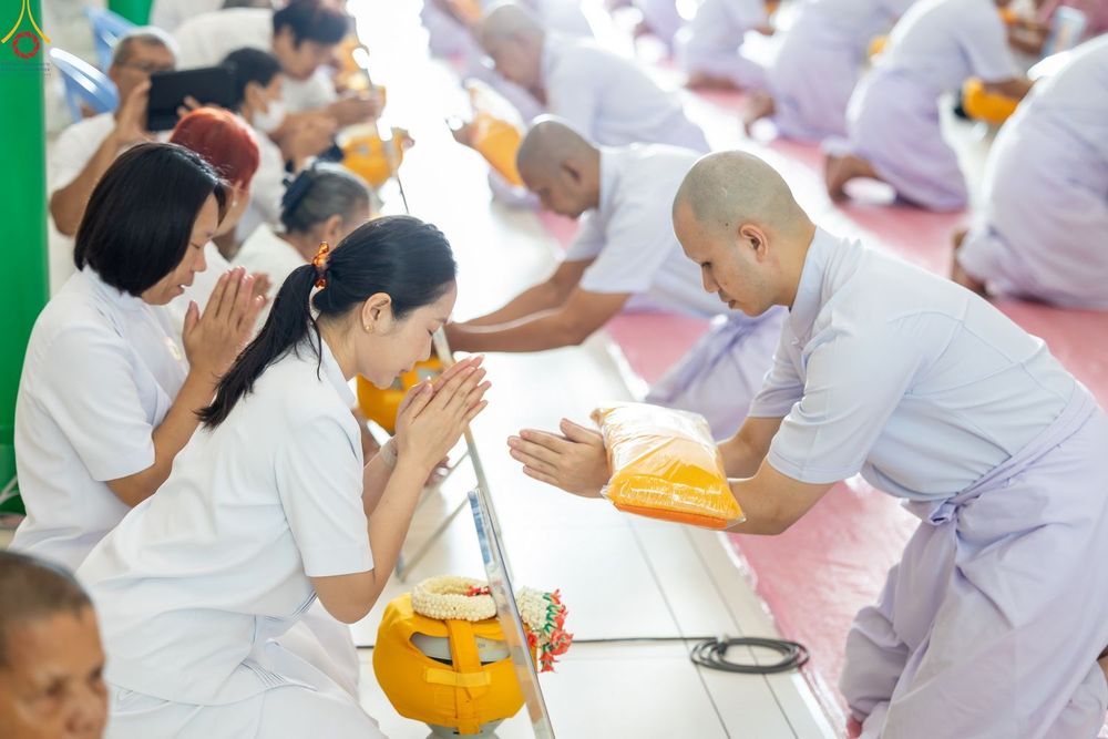 หญิงสาวในชุดสีขาวกำลังประนมมือถวายผ้าไตรแด่นาคที่กำลังจะอุปสมบทในพิธีทางศาสนา