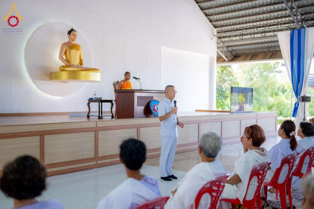 วิทยากรชายในชุดขาวกำลังบรรยายให้ผู้เข้าร่วมอบรมในชุดขาวฟังภายในอาคารปฏิบัติธรรม