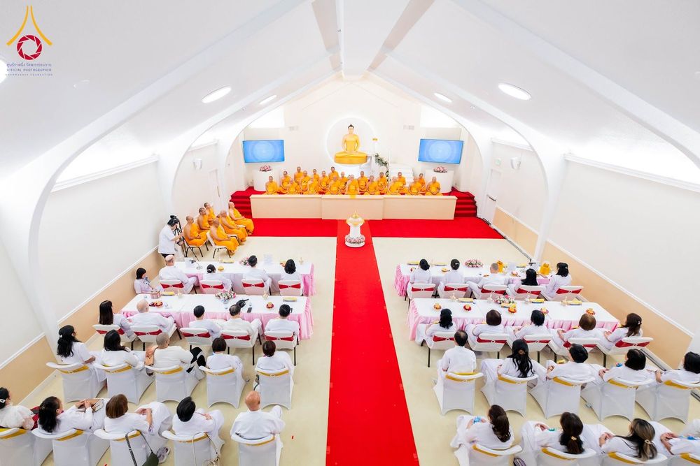 พระภิกษุสงฆ์และสาธุชนชุดขาวร่วมพิธีทางศาสนาภายในอาคารปฏิบัติธรรมที่มีพระประธานเป็นศูนย์กลาง