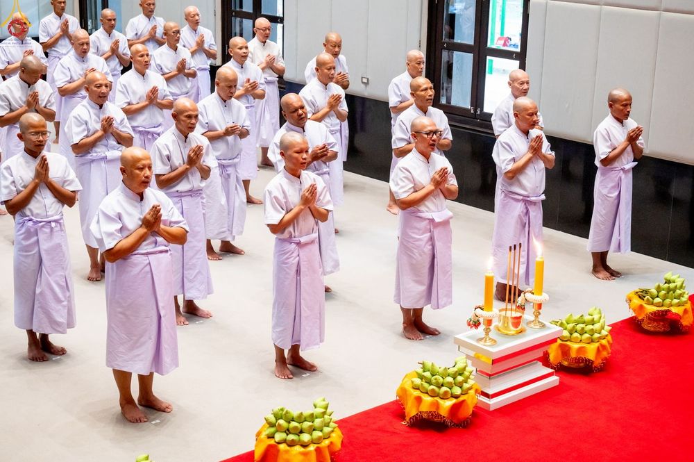 กลุ่มผู้เข้าร่วมพิธีบรรพชาอุปสมบทในชุดสีขาวกำลังยืนพนมมืออย่างสงบภายในอาคาร
