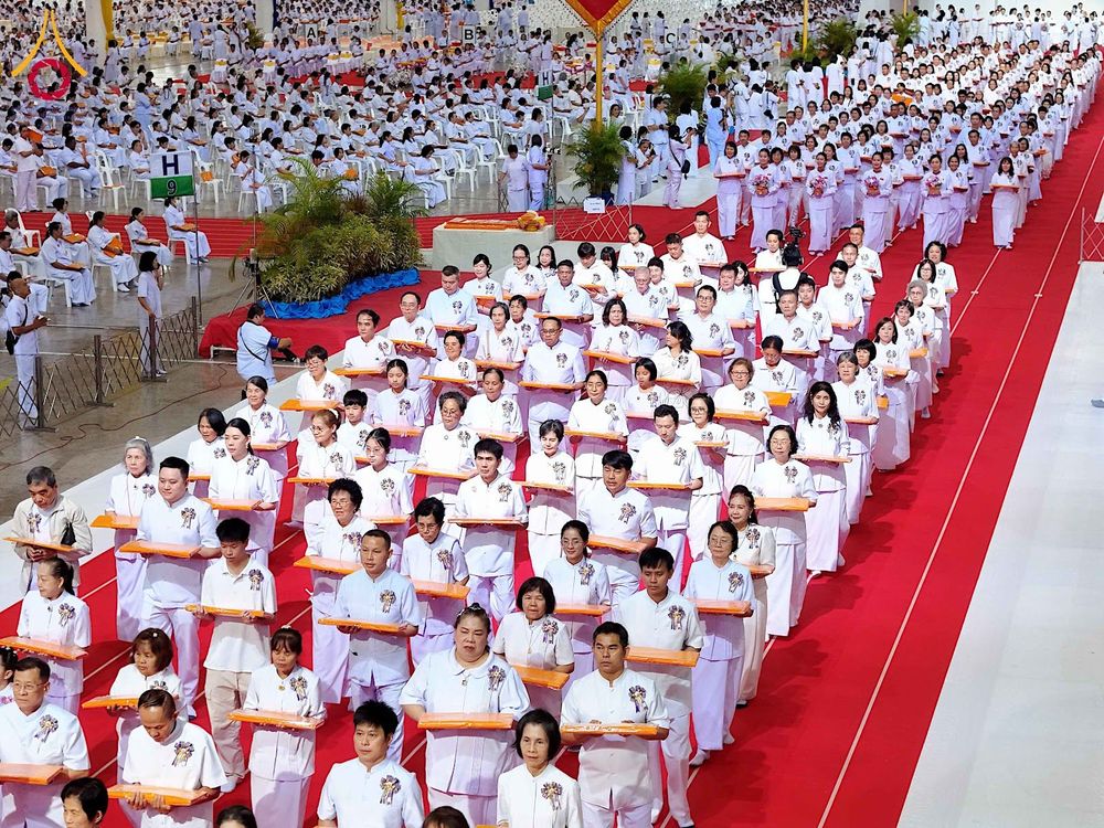 กลุ่มพุทธศาสนิกชนในชุดขาวเดินแถวถือพานผ้าไตรในพิธีทอดผ้าป่าภายในอาคารขนาดใหญ่